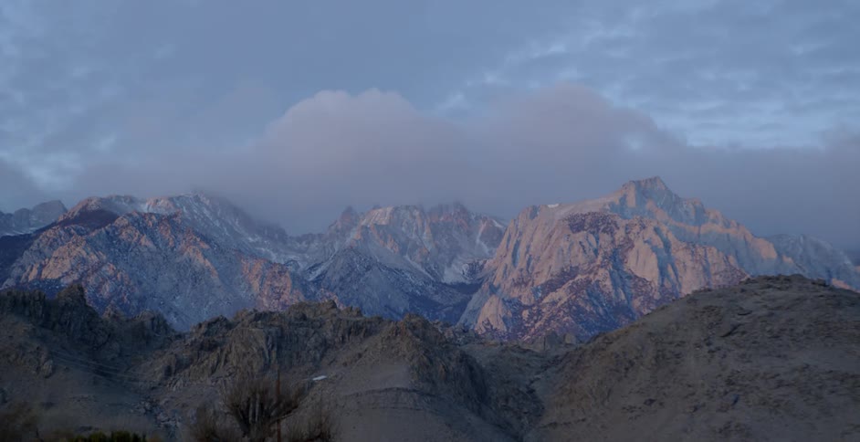 Clouds float over snowy mountains at sunrise