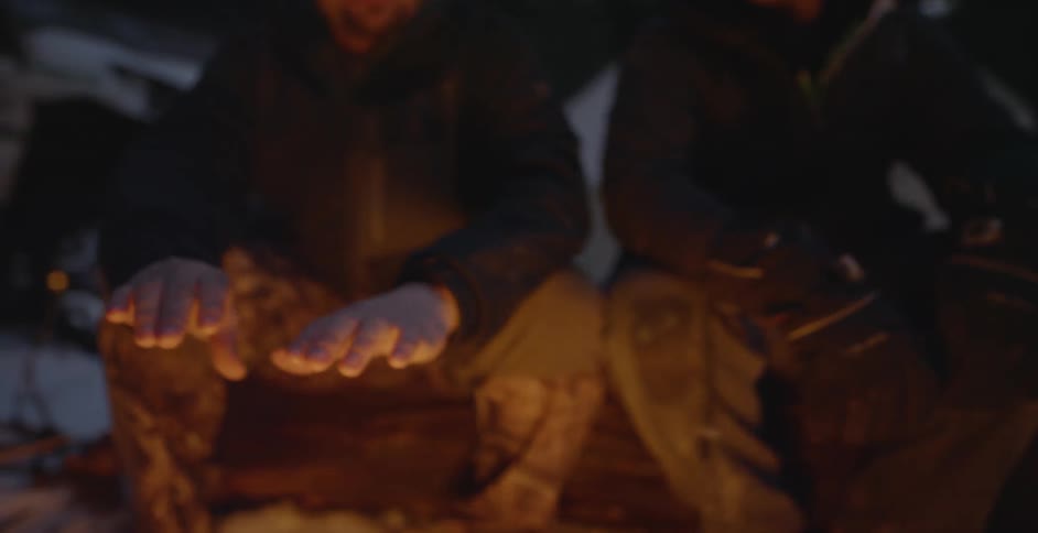 A group of men warm their hands by a fire