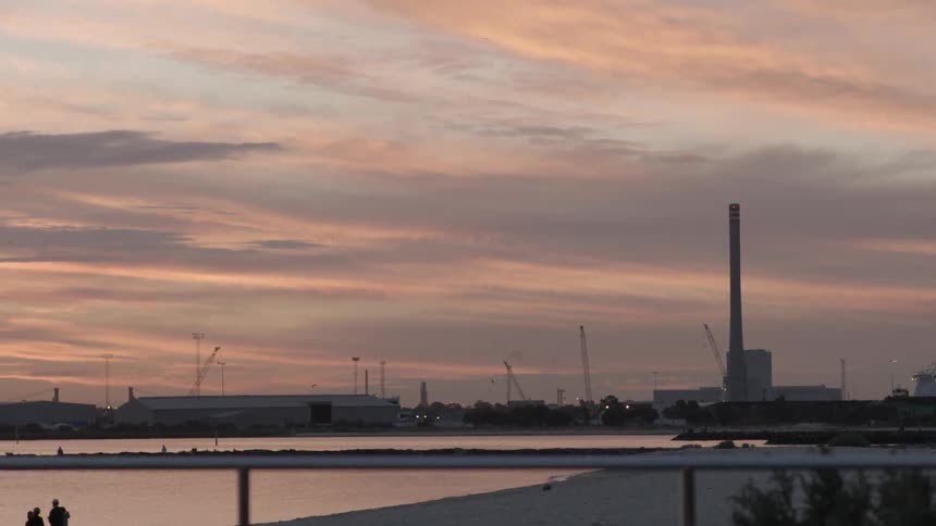 The sun sets over a shipping port by the water