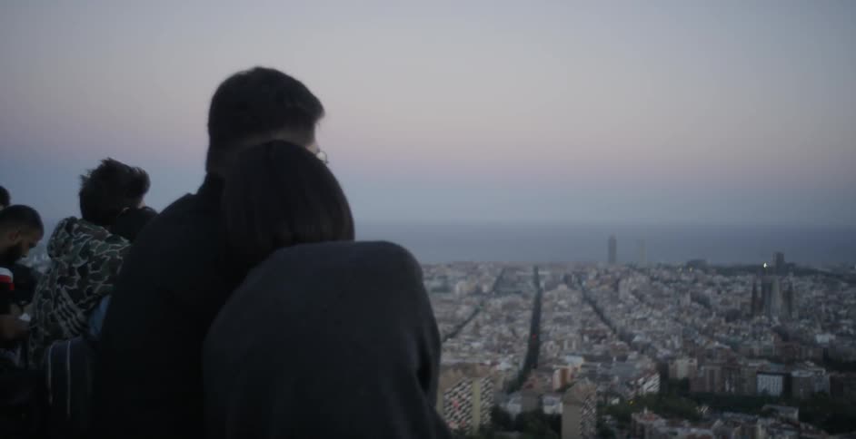 Men and women cuddle as they look out over a railing at a large city below
