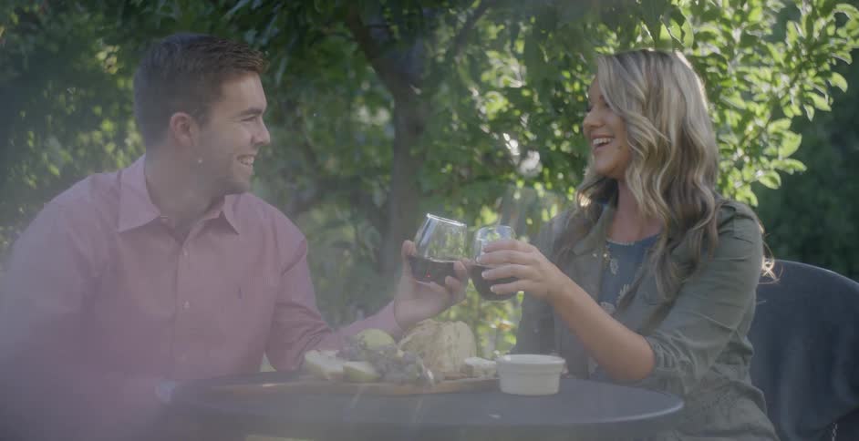 A man and woman smile and toast their drinks