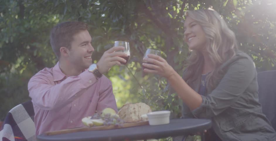 A man and woman toast wine glasses outside