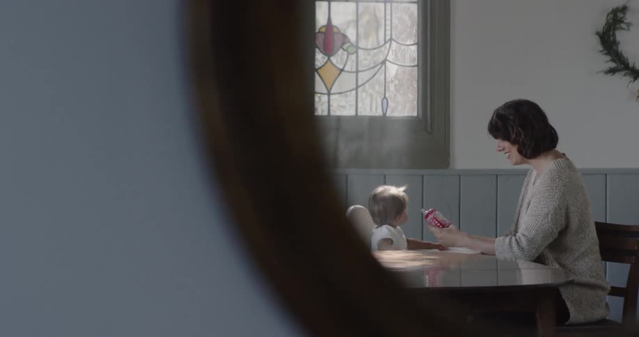 A woman is sitting at a kitchen table feeding her baby
