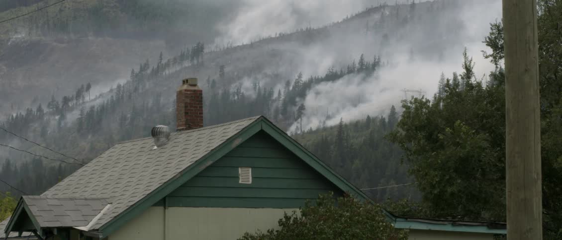 Smoke rises up from hills behind a cabin