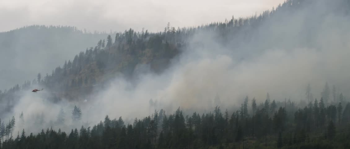 An helicopter flies over a wildfire in the mountains