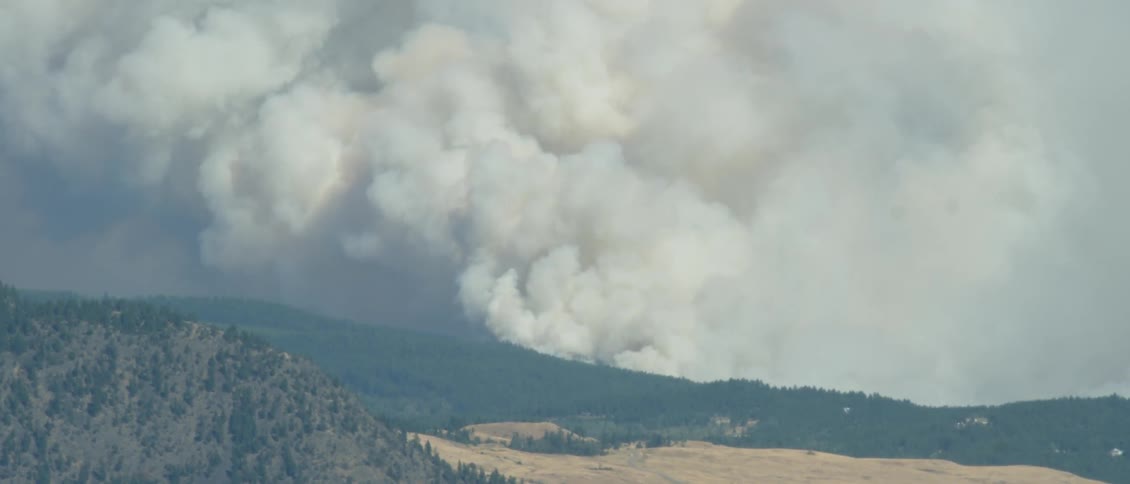 Smoke billows over tree covered hills