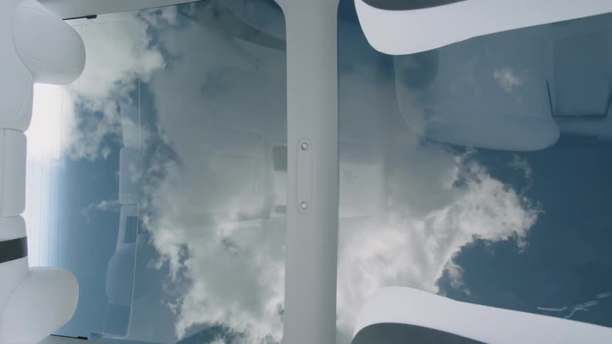 Clouds swirl overhead through a glass roof in a car
