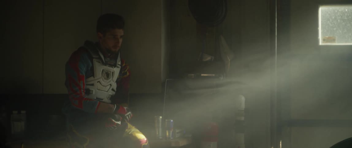 A young man is wearing motorcycle protective gear and is sitting in a darkened room