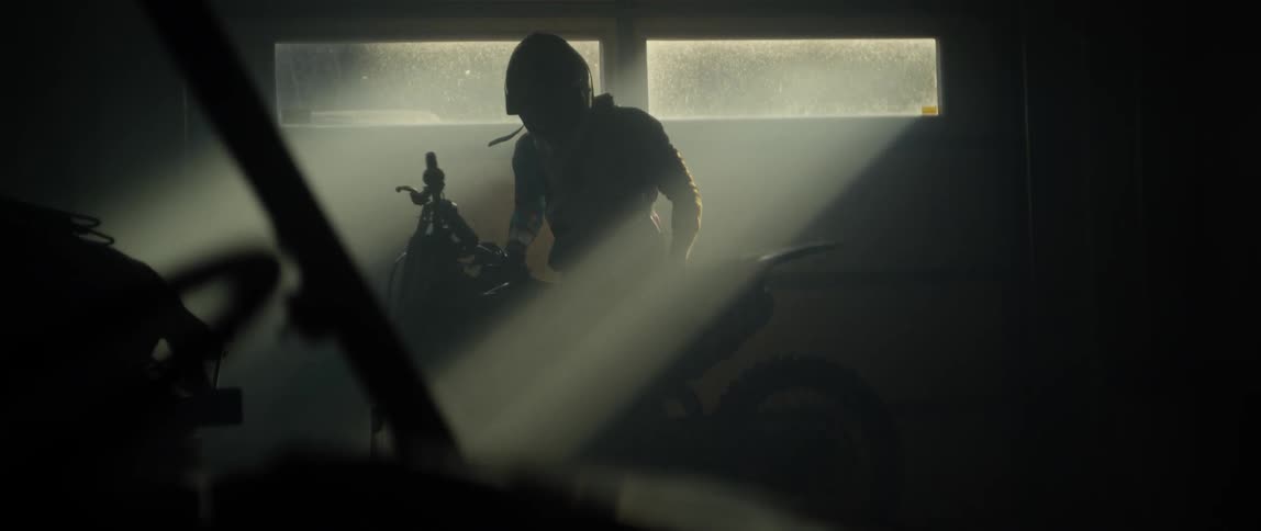 A man is lifting a dirt bike off a stand and rolling it out of a garage