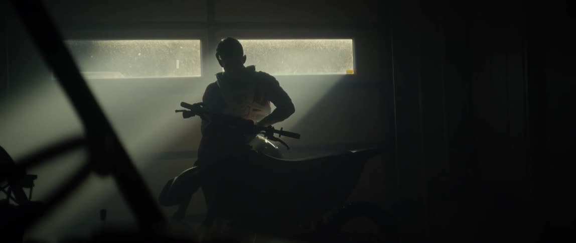 A man is picking up a motorcycle helmet and putting it on inside a garage in daylight