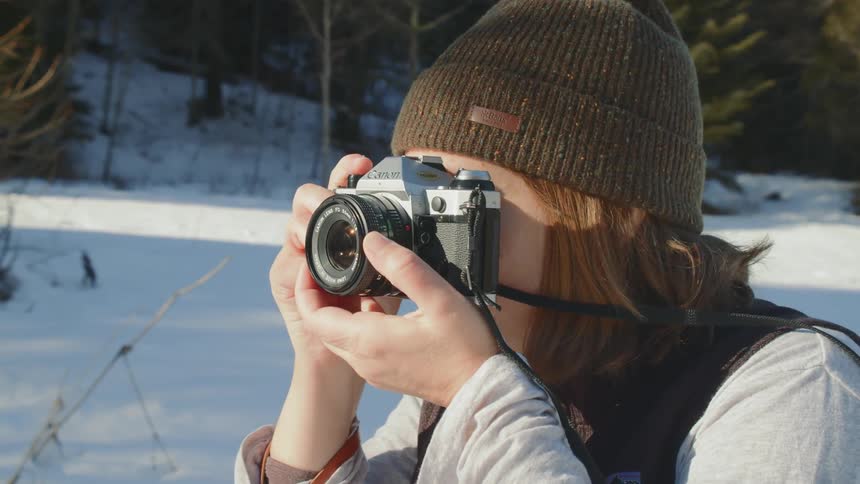 A woman takes a photograph in a snowy forest