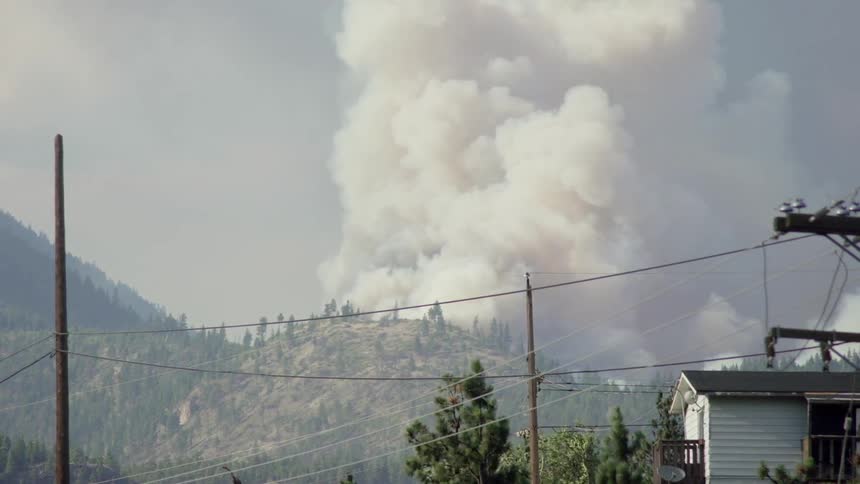 Smoke rises up from behind tree covered mountains
