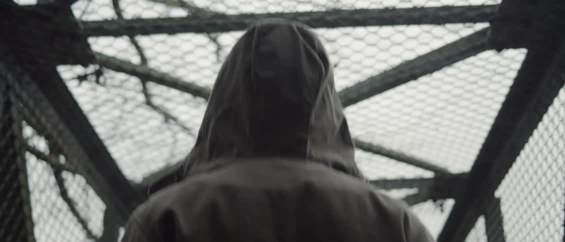 A person with their hood up walks through a gated pedestrian walkway