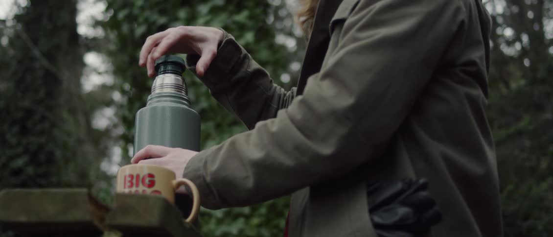 A man is opening a thermos outside in a natural setting