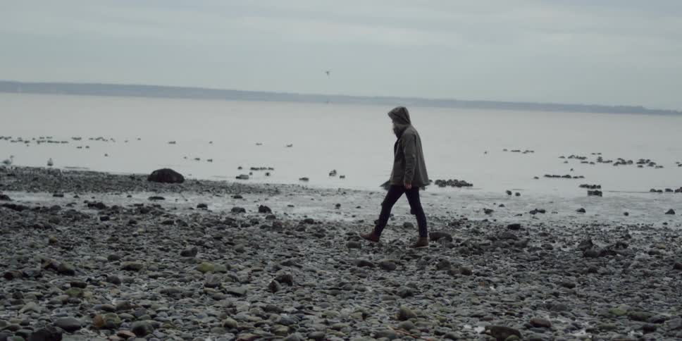 A woman walks on the rocky shore