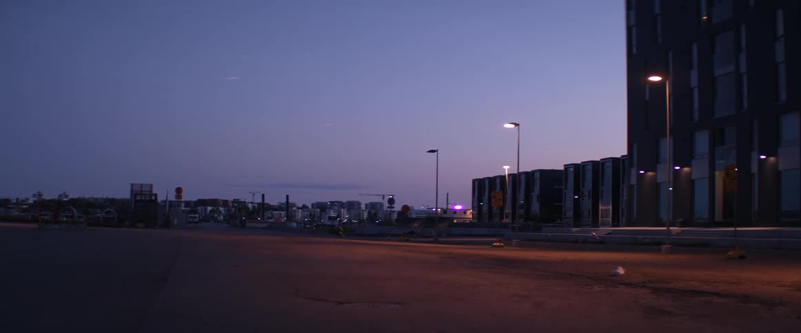 Modern industrial buildings line a deserted asphalt field during a clear summer evening.