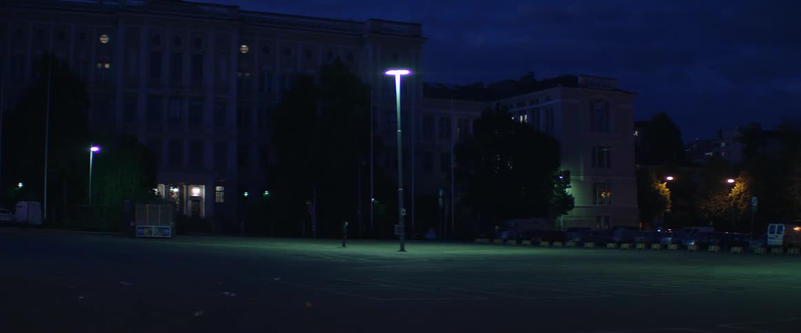 Bright green light shines down on a deserted public plaza near dark buildings.