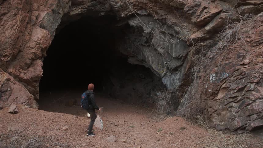 A man walks up to a cave while holding a lantern