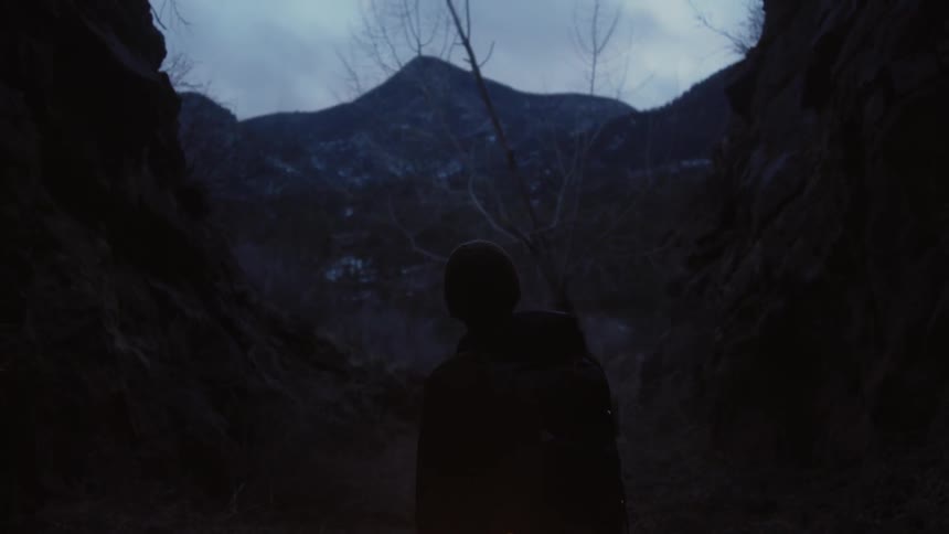 Man standing in a dark area between hills in the wilderness on a cloudy day