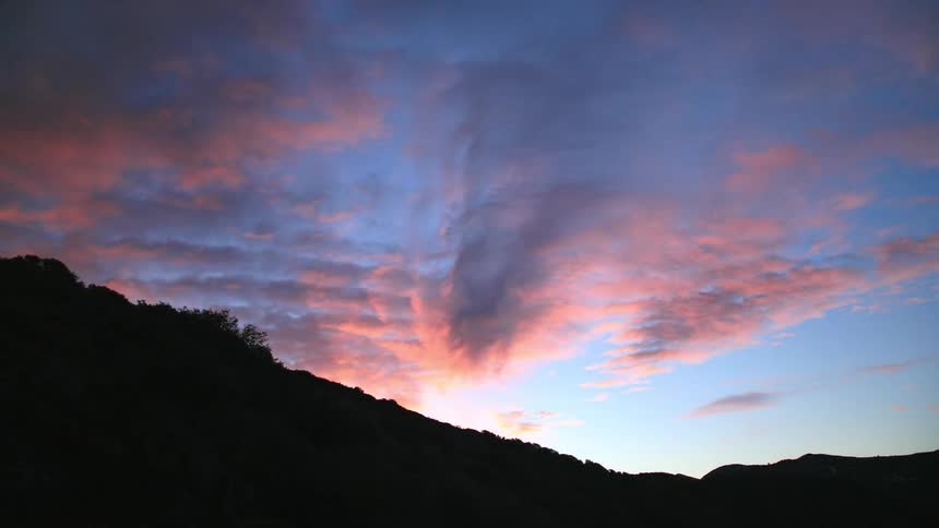 Clouds float over a hill at sunset