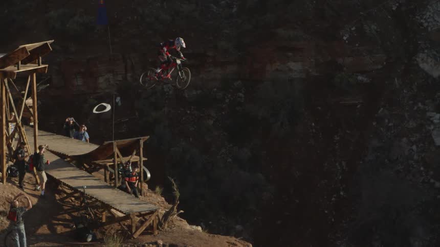 Man rides his bike off a ramp and does a jump onto a trail