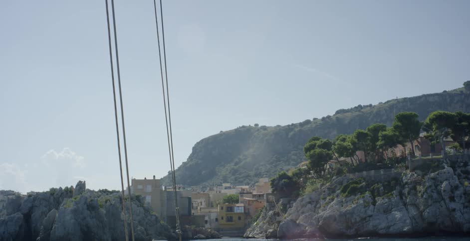 A boat floats in the ocean near coastal cliffs and a village