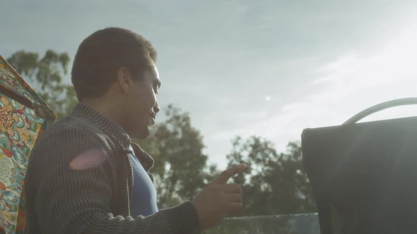 Man talks and laughs in front of a grill on a sunny day
