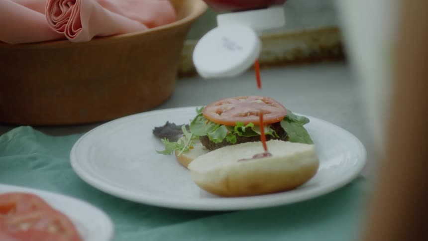 Person places ketchup on the bun of a burger