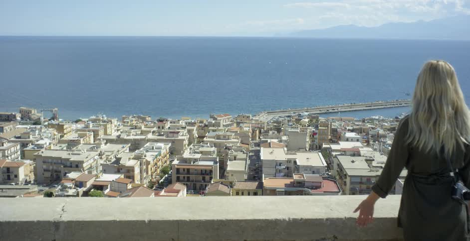 Woman walking towards lookout over city and ocean on sunny day