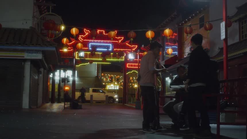 People sit at outdoor benches and eat in chinatown at night