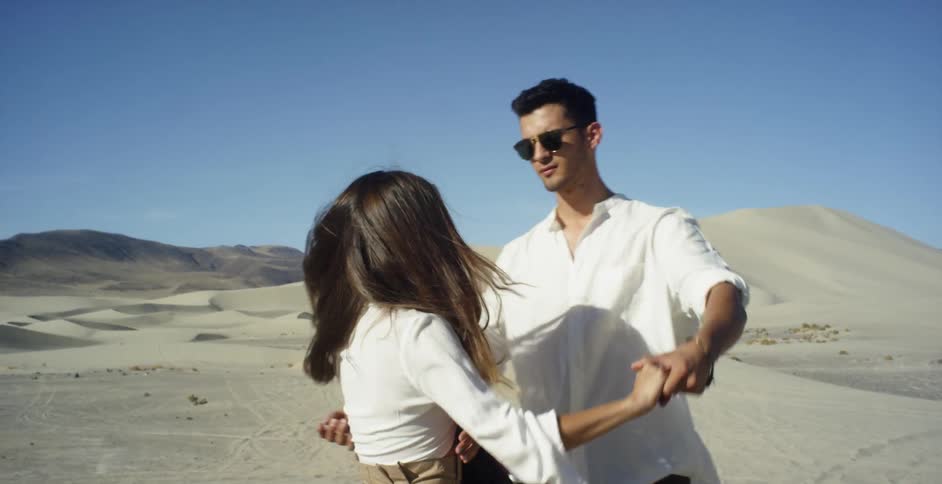 Man and woman are dancing near sand dunes on sunny day
