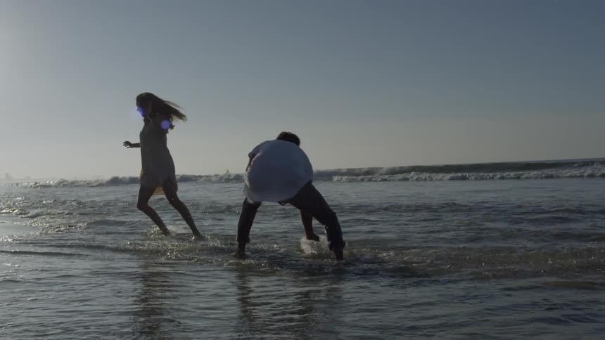 Couple are playing and splashing in the waves at a beach in daylight