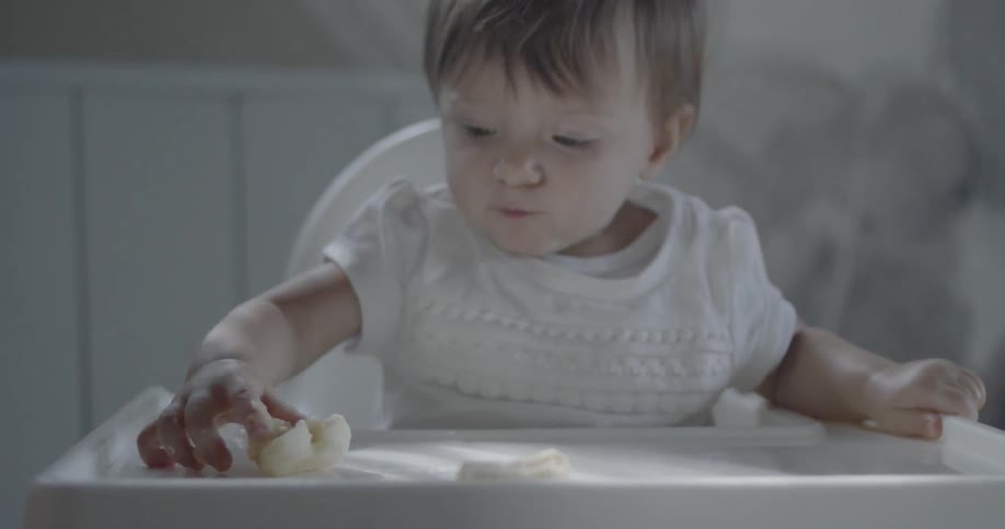 A young child plays with its food in a high chair