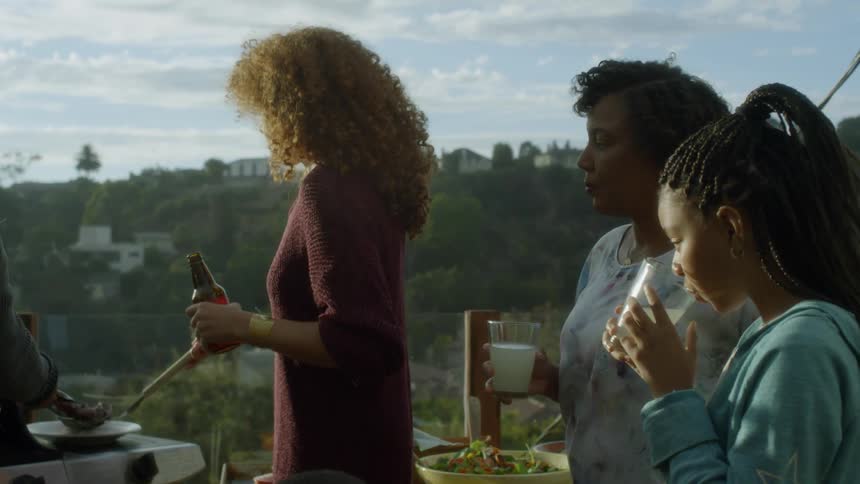 Three women stand outside as one grills and the other two drink out of glasses