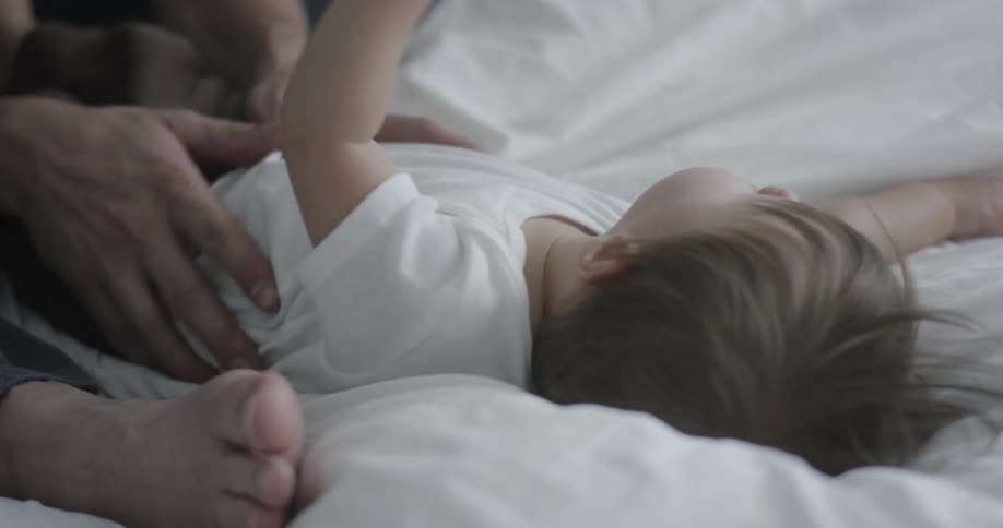 A baby and a daddy are playing in the bed together