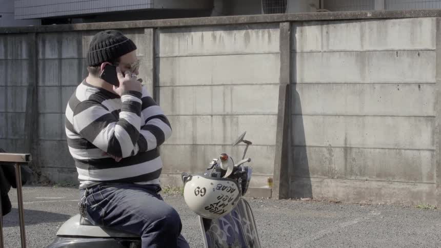 Man with moped sits on park bench talking on the phone