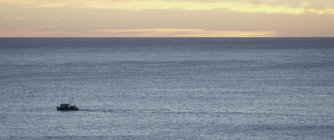 A boat sails on the ocean at sunset