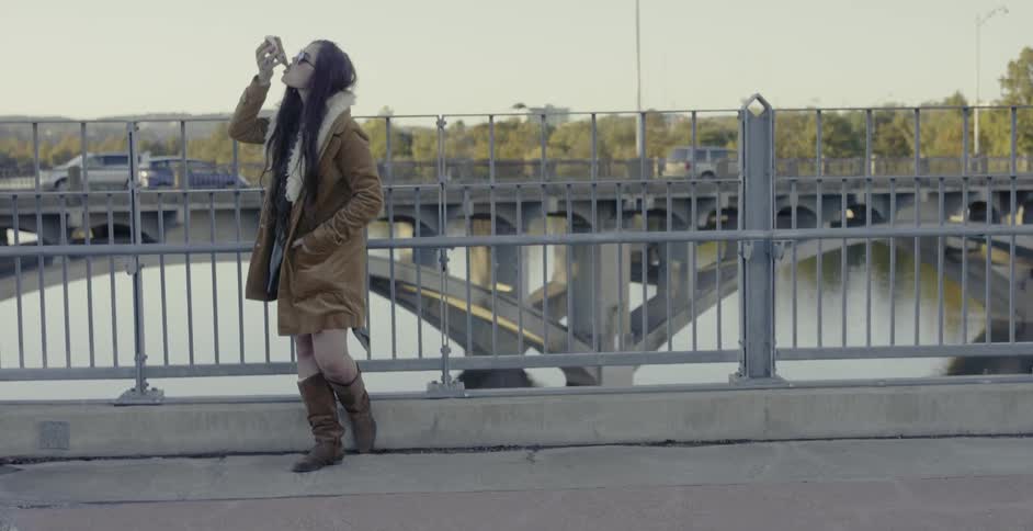 A woman eats an ice cream cone on a city bridge