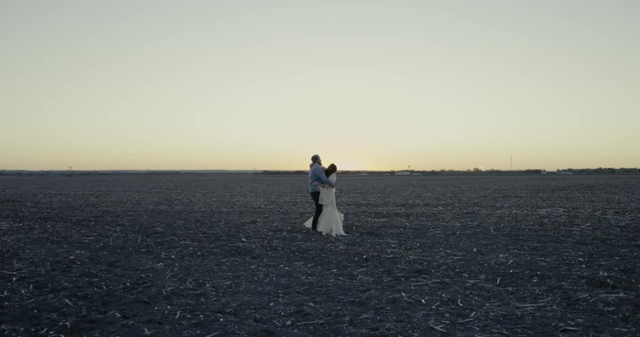 A man and woman hug in a rural field at sunset