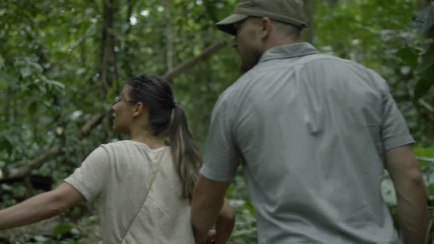 A man and woman hold hands while walking in a forest
