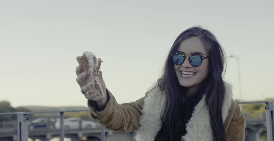 Woman standing on balcony hold out a melting ice cream cone and laughs