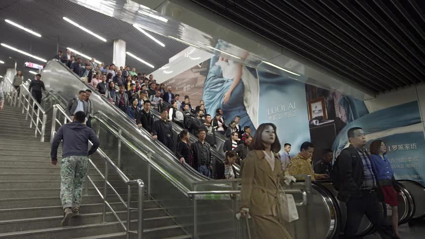 Crowd of people ride down an elevator and some walk up or down the steps