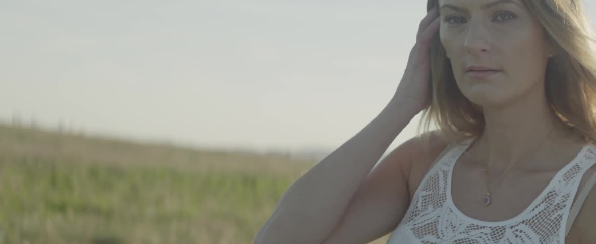 Woman stands on hillside with wind blowing in her hair