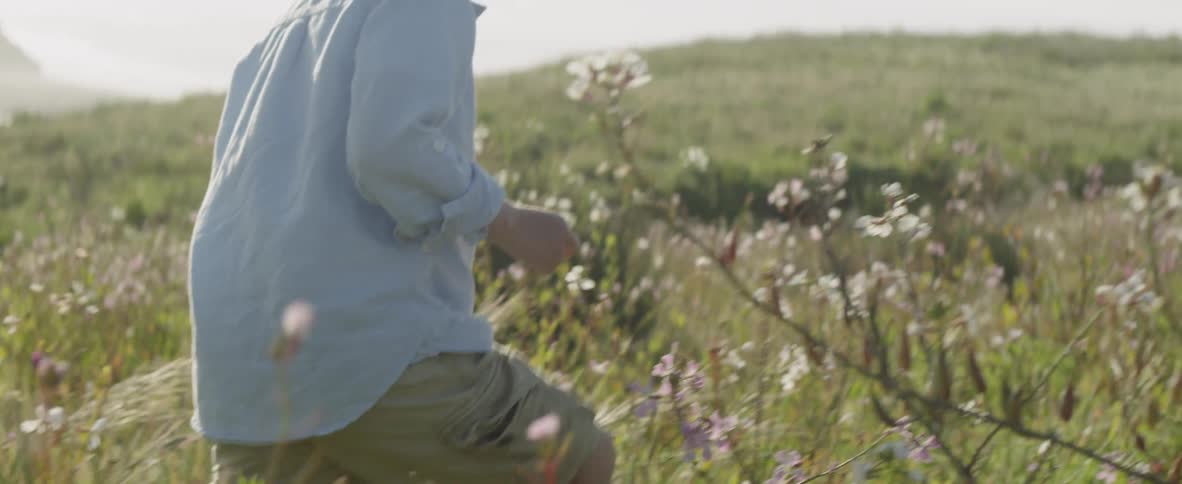 A boy is walking through a field of grass and flowers in daylight