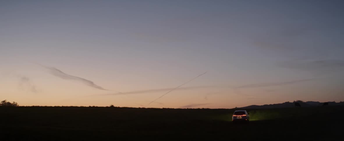 Vehicle driving towards a soft sunset with trailing clouds