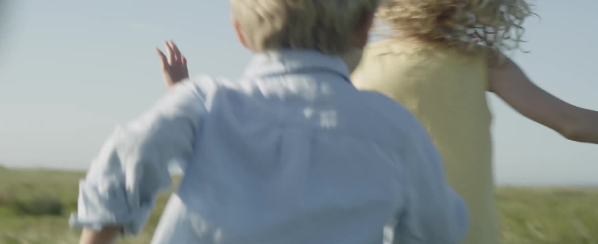 Two children run and play in a grass field