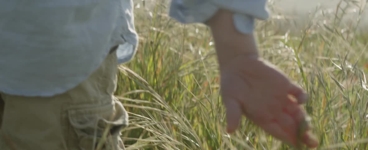 A boy standing outside grabs some weeds and twists them around