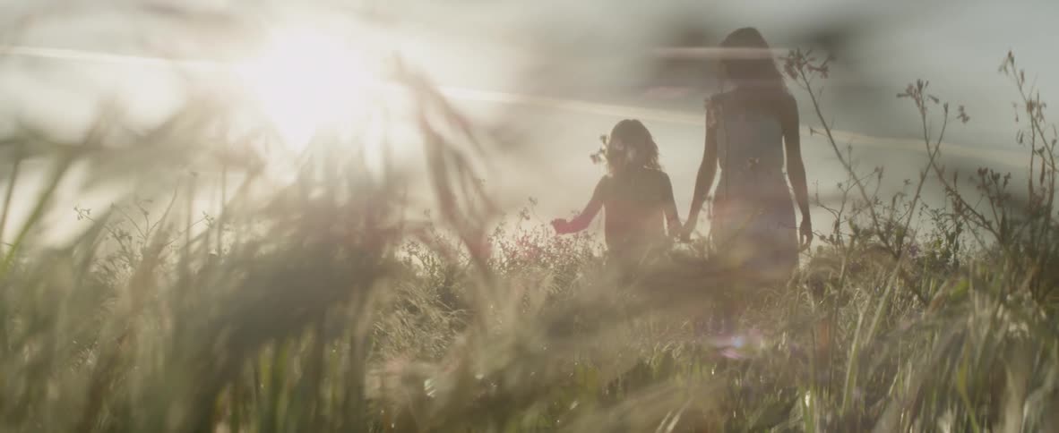 A woman and girl are walking through a field with flowers in daylight