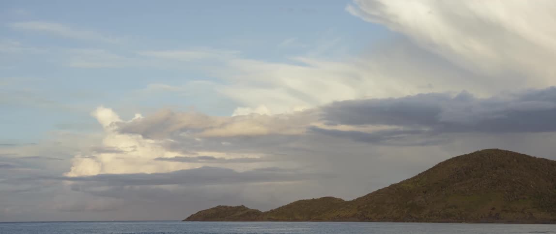 A long shot taken from a beach of the horizon, a hilly peninsula, and the distant clouds
