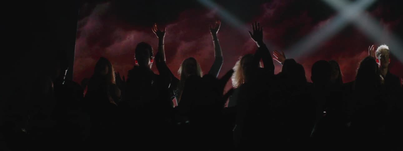 Members of a choir are raising their hands as they sing in front of projected images